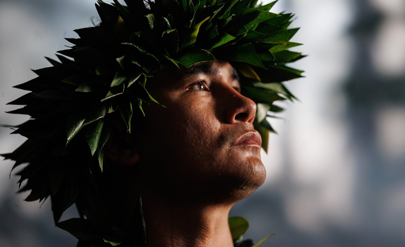 Close-up of a man wearing a green leaf head lei, looking upward into soft light